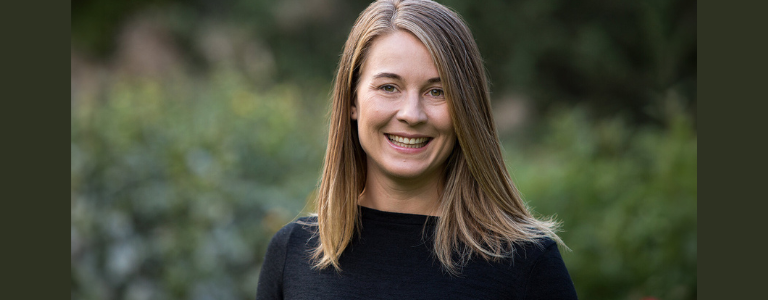 Dr. Maaike Canrinus stands in front of foliage, smiling at the camera.